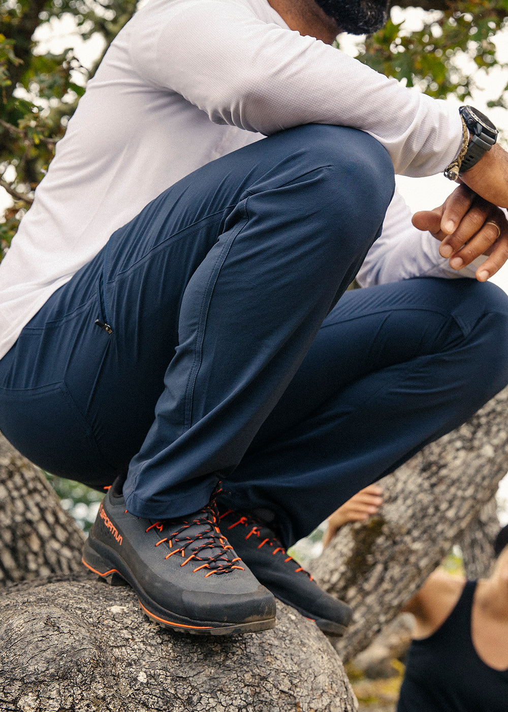 Man crouches on a branch of a tree he climbed while wearing Outdoor Research Ferrosi Pants in Dark Navy.